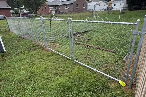 Galvanized chain-link fence gate with decorative metal scrollwork on top, set in a grassy yard.