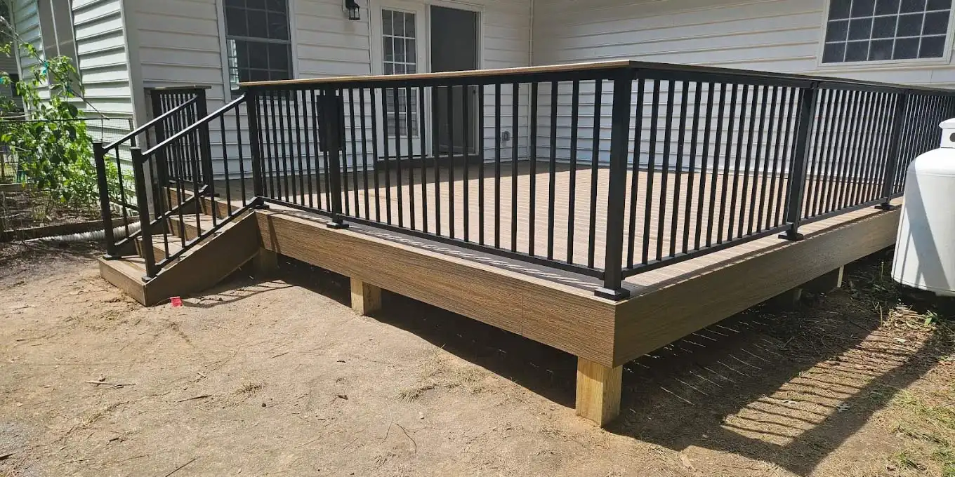 Exterior view of a spacious brown composite deck enclosed by black metal railings against a white vinyl-sided home.